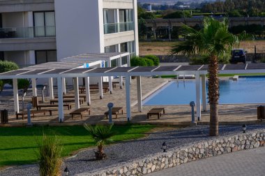 Kıbrıs 'ta lüks bir konut kompleksinde havuz etrafında şemsiyeleri olan rahat güneş pansiyonları. Güneşin altında dinlenmek için mükemmel bir yer..