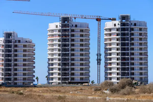 Açık mavi gökyüzüne karşı yükselen üç yüksek konut kulesi devam eden inşaat çalışmalarını gözler önüne seriyor..