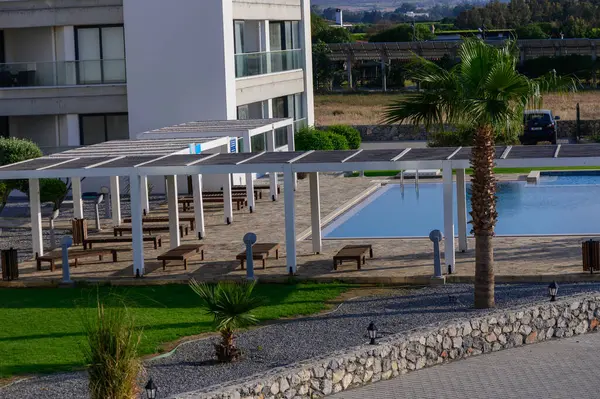 Kıbrıs 'ta lüks bir konut kompleksinde havuz etrafında şemsiyeleri olan rahat güneş pansiyonları. Güneşin altında dinlenmek için mükemmel bir yer..