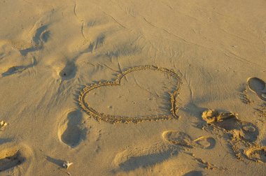 Güzel bir kalp şekli sıcak kuma kazınmış, sakin bir kumsalda yumuşak ayak izleriyle çevrili..