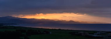 Gün ışığı söndükçe, denizin üzerinde nefes kesici bir renk dizisi belirir, engebeli dağları aydınlatarak manzaraya yumuşak gölgeler bırakır. Huzurlu bir güzellik anı.