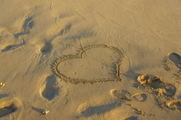 Güzel bir kalp şekli sıcak kuma kazınmış, sakin bir kumsalda yumuşak ayak izleriyle çevrili..