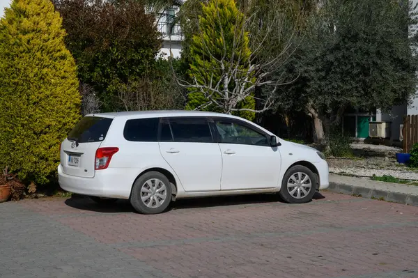 Gaziveren Kıbrıs Rum Kesimi 01.03.2025 Huzurlu, güneşli bir yerleşim bölgesinde canlı bir çalılığın yanında beyaz bir steyşın vagon dinleniyor.