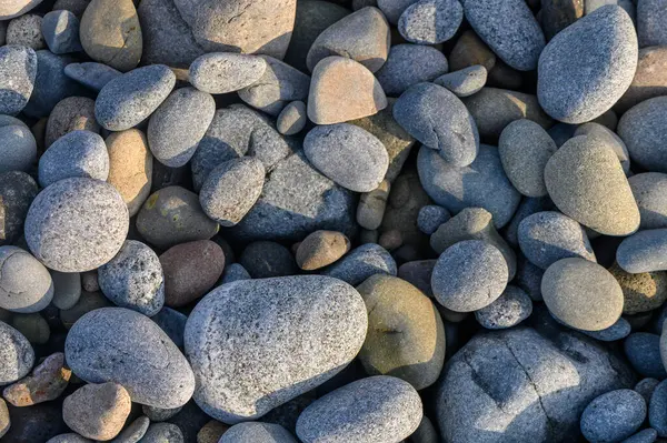 Gri taşlar, güneş batarken sakin nehir kıyısını örtüyor ve huzurlu bir atmosfer yaratıyor..