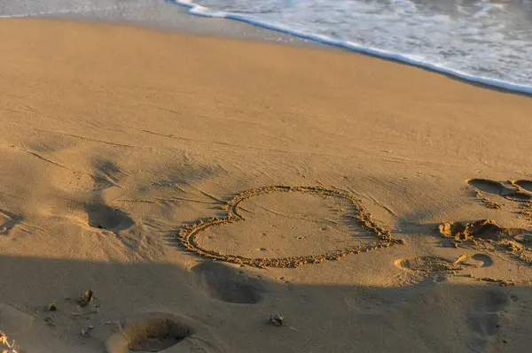 Kumlu bir kalp kıyı şeridinde usulca kıvrılır dalgalar alacakaranlıkta sahili nazikçe öperken.