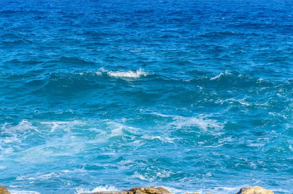 Turkuaz dalgalar, yaz güneşi altında parıldayan kayalık kıyı şeridine hafifçe çarpar. Huzur uyandırır..