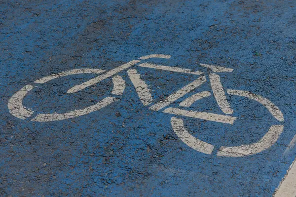 Canlı bir bisiklet sembolü, kentsel alanda canlı bir mavi kaldırıma karşı duruyor, bir bisiklet yolunu vurguluyor ve şehirde çevre dostu ulaşım seçeneklerini teşvik ediyor.