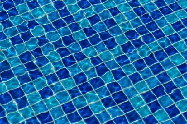 Parlak güneş ışığı altında, titreyen dalgalar, sakin bir yüzme havuzunun mavi fayanslı yüzeyinde dans eder..