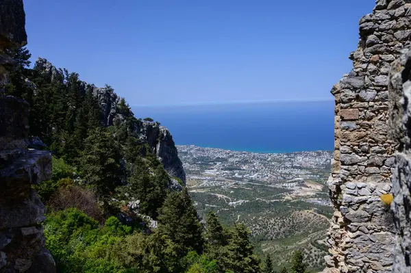 Kuzey Kıbrıs 'taki St. Hilarion Şatosu' ndaki taş çerçeveli bir pencereden dağların ve kıyı şeridinin görüntüsü.