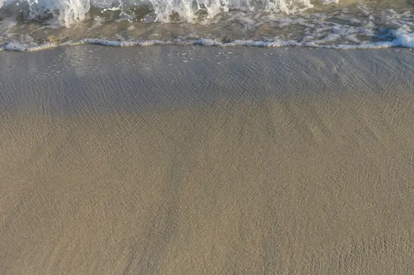 Yumuşak dalgalar, huzurlu bir sahil manzarasında sabahın erken saatlerindeki ışığı yansıtan pürüzsüz kumların üzerinde süzülür..