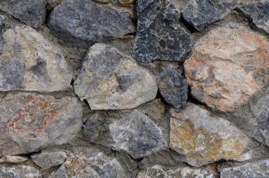 Kalıplı bir taş duvar, açık bir bahçe için kırsal bir zemin oluşturan güzel bir renk ve desen dizisi sergiliyor. Güneş ışığı her bir eşsiz taşı vurgular, derinlik yaratır..