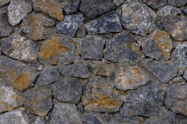 Engebeli bir taş duvar, eşsiz şekilli kayalar ve toprak renklerden oluşan karmaşık bir düzenleme sergiliyor..