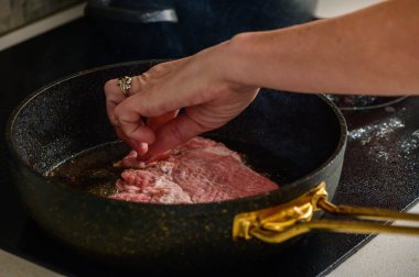 Bir el, sıcak, davetkar bir mutfakta, evde yemek pişirmenin zevkini uyandıran bir bifteği nazikçe mevsimlendirir..