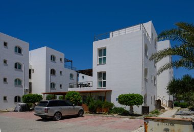 Kıbrıs 'ta güneşli bir sitede beyaz konutun yakınına park edilmiş modern gümüş renkli SUV..