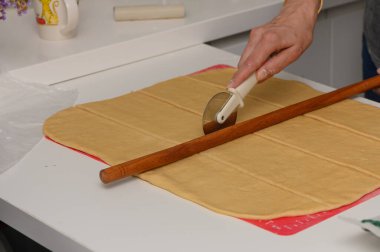 Yumuşak hamuru eşit oranda kesen bir kadının yakın çekim görüntüsü. Un kaplı bir yüzeyde yuvarlak bir pizza kesicisi kullanıyor..