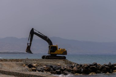 Kıbrıs Rum Kesimi 'nde güneşli bir günde Akdeniz kıyısı yakınlarında sarı bir kazıcı çalışıyor