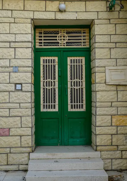 Parlak yeşil ahşap bir kapısı ve beyaz boyalı duvarları olan tipik bir Kıbrıs Rum evinin klasik girişi.