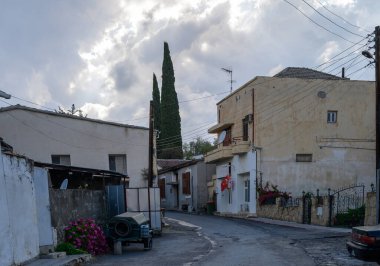 Kıbrıs 'ta sakin ve güneşli bir sokak. Geleneksel evler, park edilmiş arabalar ve açık mavi gökyüzü altında Akdeniz bitkileri..