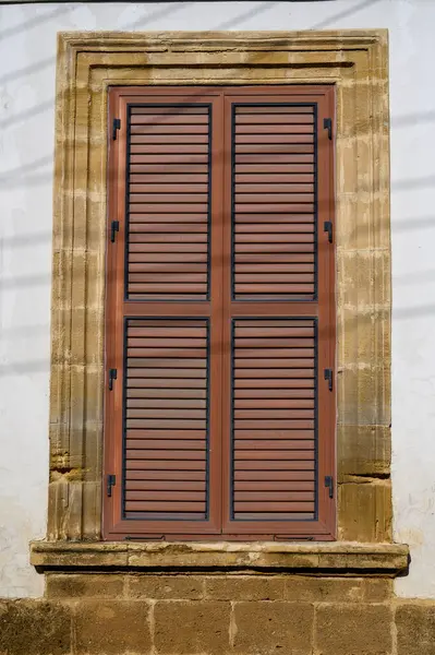 Kıbrıs 'ın bir köyünde beyazlatılmış bir duvarda ahşap panjurlu klasik Akdeniz tarzı pencere..