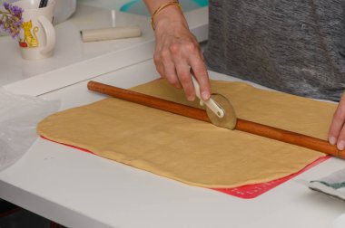 Bir kadın pizza keskisi kullanarak hamuru dilimler ve onu pişirmeye hazırlar..