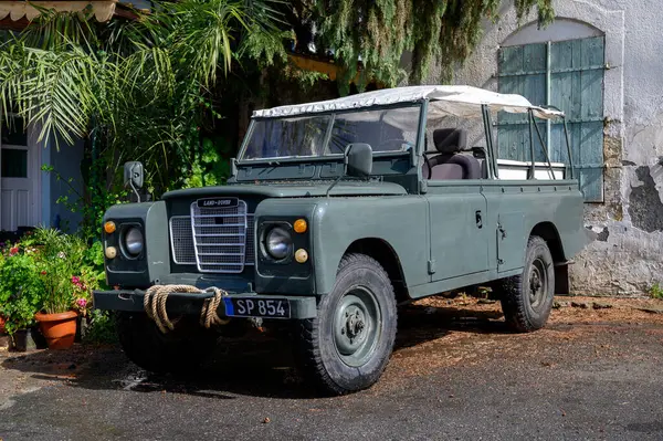 Kıbrıs 'ta sakin bir sokağa park etmiş eski yeşil Land Rover klasik tasarım ve Akdeniz kentsel atmosferini sergiliyor.