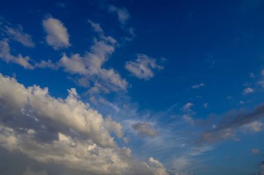 Pofuduk beyaz bulutlar açık mavi gökyüzünde süzülüyor. Tasarım, seyahat ve yaratıcı kompozisyonlar için barışçıl ve parlak doğal arkaplan.