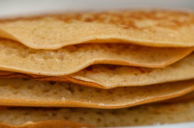 Beyaz bir tabakta servis edilen, üzerinde şerbet ve tereyağı olan, kahvaltıda eğlenmeye hazır bir yığın altın, tüylü krep..