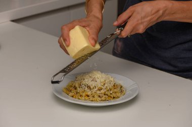 Dişi bir aşçı peyniri yeni hazırlanmış makarnanın üzerine ızgara yapar. Ev mutfağında lezzetli ve iştah açıcı bir yemek yapar..