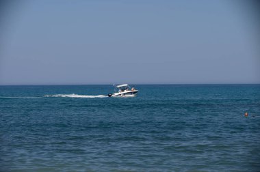 İnsanları taşıyan bir motorlu tekne, Kıbrıs yakınlarındaki berrak mavi sulardan geçiyor. Hafif dalgalarla parlak güneş ışığı altında yakalanıyor.