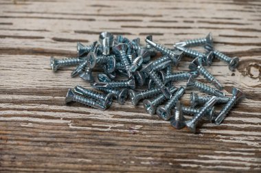 Metal çatı vidaları eski ahşap bir masaya saçılmış, DIY, inşaat ve donanım fotoğrafçılığı için ideal.