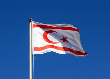 Kuzey Kıbrıs 'ın kırmızı ve beyaz bayrağı bulutlu mavi gökyüzüne doğru uzun bir bayrak direğinde dalgalanıyor.