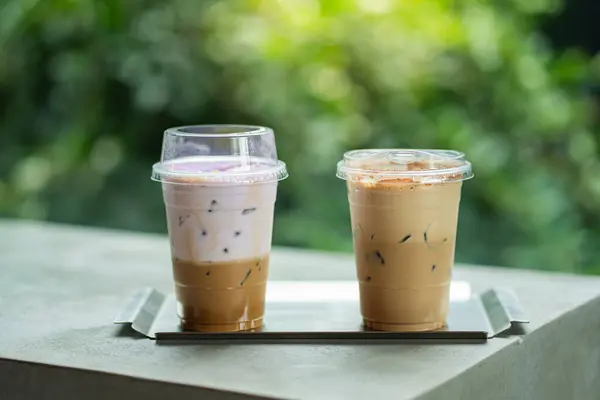 Bir bardak buzlu kahveyi taro sütlü ve buzlu kapuçinoyla yaz terasında bir kahve dükkanının çiğ çimento masasında, menü fotoğrafçılığıyla kapatın..