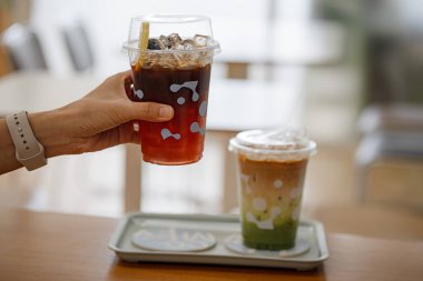 Ellerinde limonlu buzlu çay ve kafedeki ahşap masada kibrit yeşil çay tutan genç kız ve oğlanın elleri..