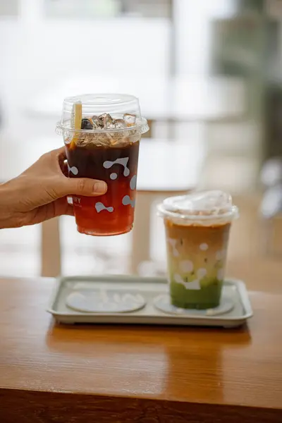 Elinde limonlu buzlu çay ve kafedeki ahşap masada kibrit yeşil çay tutan genç kızın elleri..