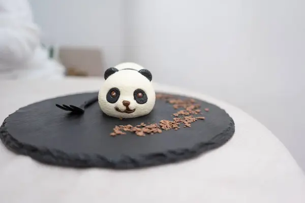 Kafedeki beyaz masada siyah tabakta panda keki.