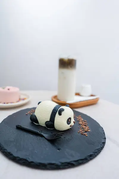 Panda keki, çiçek pastası ve kavrulmuş yeşil çay. Kahvede beyaz masada siyah bir tabakta latte. Düz yemek konsepti..