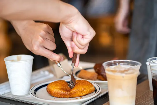 Seçici odaklanmış eller, elinde bir bardak buzlu kahve tutan ve sabah kafede karton kutuda pişmiş tatlı tarçınlı sandviçi bulanıklaştıran kişi..