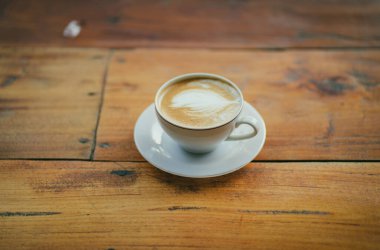  Düz beyaz kahve kupası, ahşap masada kalp şeklinde latte sanatı. 