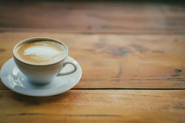 Düz beyaz kahve kupası, ahşap masada kalp şeklinde latte sanatı. 
