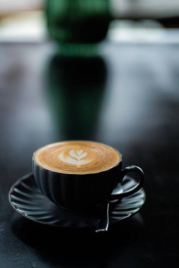 Siyah bir fincanda siyah ahşap masada sütlü kahvenin yan görüntüsü.