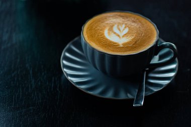 Siyah bir fincanda siyah ahşap masada sütlü kahvenin en üst görüntüsü.