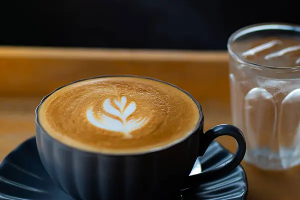 Siyah bir fincanda siyah ahşap masada sütlü kahvenin yan görüntüsü.