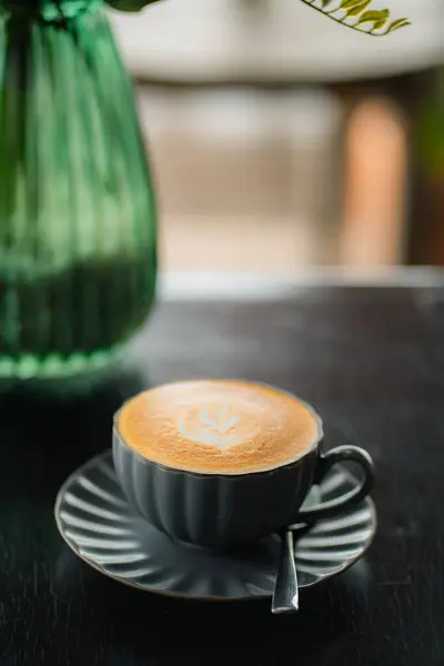 Siyah bir fincanda siyah ahşap masada sütlü kahvenin yan görüntüsü.