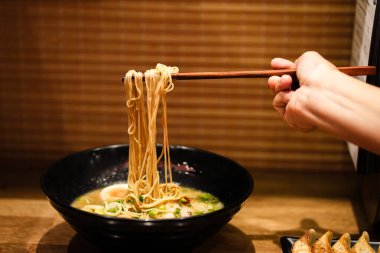Yemek çubuklarıyla meçhul bir kadın erişteli lezzetli ramen çorbası yiyor ve Ramen restoranında siyah kasede et yiyor..