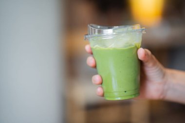 Kafe 'deki masada elinde buzlu matcha latte tutan bir kadın.