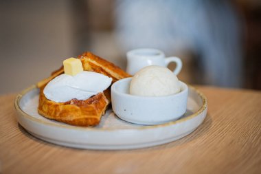 Bir tabak Belçika waffle tatlısı. Dondurma ve ahşap masada böğürtlenlerle süslenmiş..