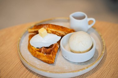 Bir tabak Belçika waffle tatlısı. Dondurma ve ahşap masada böğürtlenlerle süslenmiş..