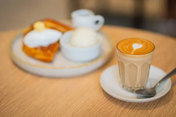 Kahve dükkanındaki ahşap masada, kahve bardağında latte sanatıyla seçici bir odak noktası. Uzay konseptini kopyala..