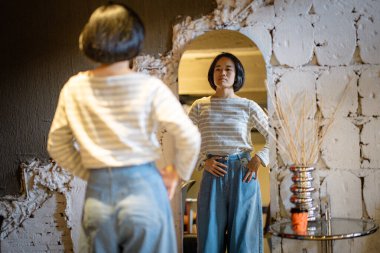 Kazaklı, kendine güvenen genç ve güzel bir kadın ve aynaya bakan kot pantolon kendisiyle gurur duyuyor.