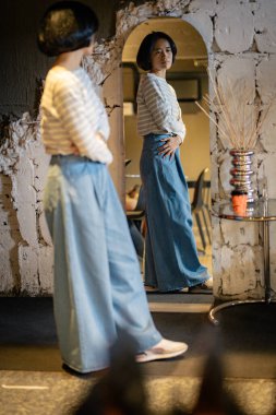 Kazaklı, kendine güvenen genç ve güzel bir kadın ve aynaya bakan kot pantolon kendisiyle gurur duyuyor.